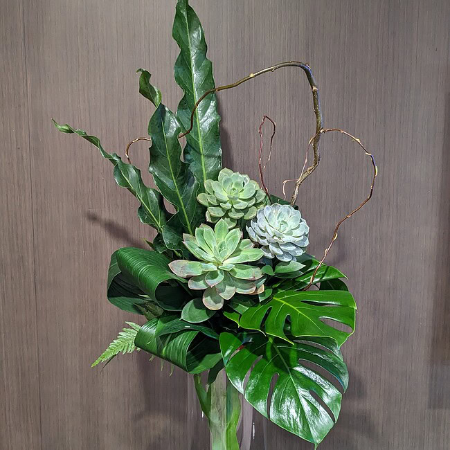 Elegant succulent and tropical leaf floral display in a glass vase.