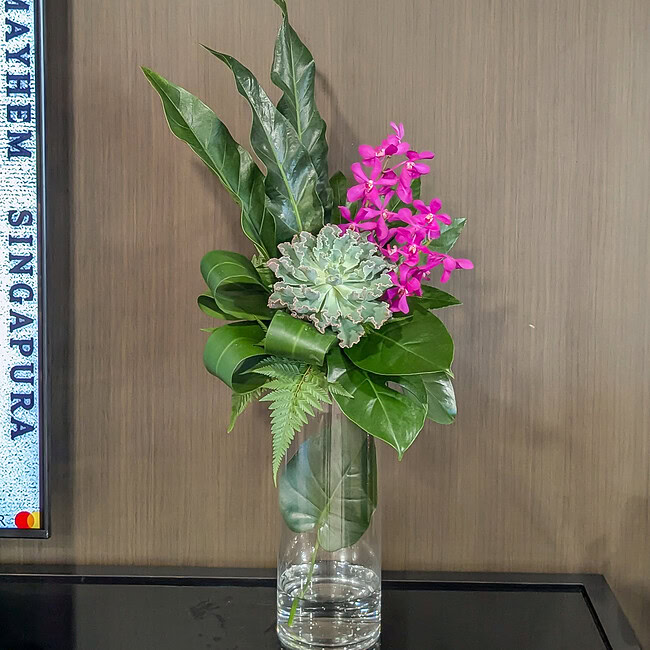 Elegant floral arrangement with orchids and greenery in a glass vase.
