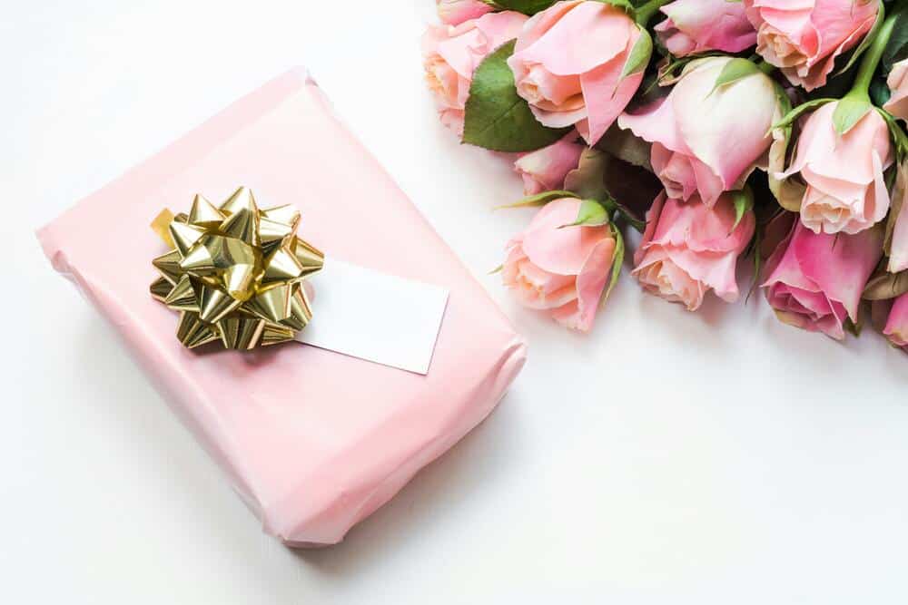Beautiful pink roses paired with a wrapped birthday gift and gold bow, perfect for celebrating birth.