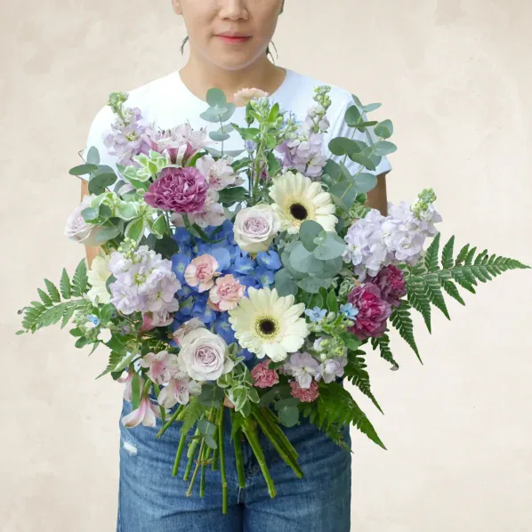 Elegant floral arrangement with pastel roses, gerbera daisies, and greenery.