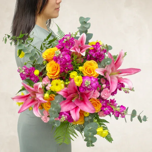 Vibrant floral arrangement with pink lilies, yellow roses, and purple blooms.