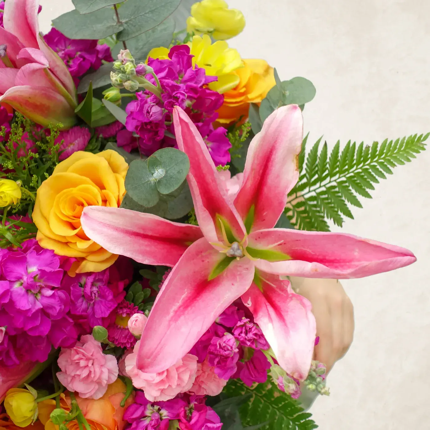 Vibrant pink lily with colorful roses and greenery in a floral arrangement.