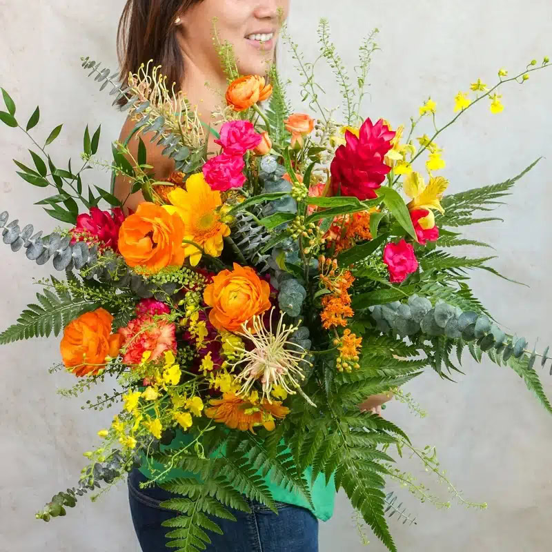 Vibrant flower bouquet featuring orange, pink, yellow blooms with lush greenery, perfect for special.