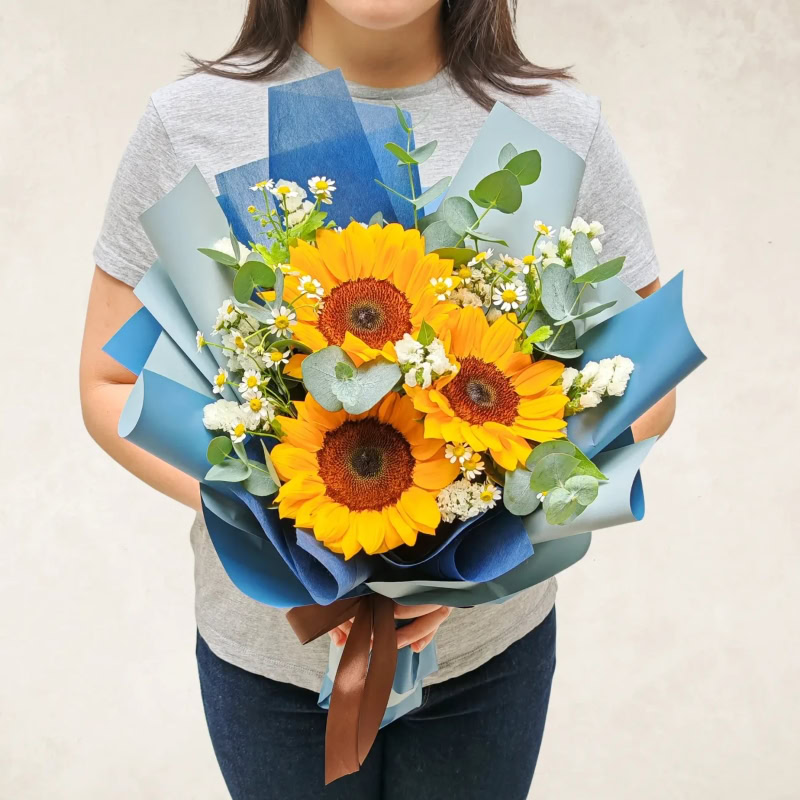 Sunflower bouquet featuring vibrant sunflowers, white filler flowers, and green foliage, wrapped in.