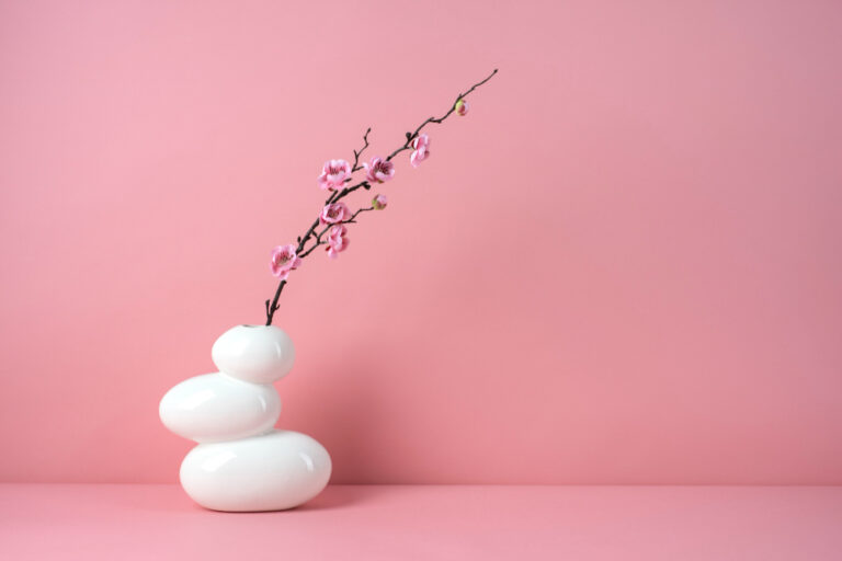 Elegant pink cherry blossom branch in minimalist white vase on pink background.