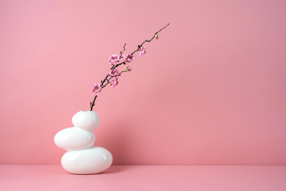 Elegant pink cherry blossom branch in minimalist white vase on pink background.